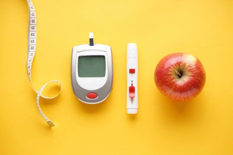 Glucose meter, lancet device, measuring tape, and a red apple on a bright yellow background, symbolizing health monitoring.